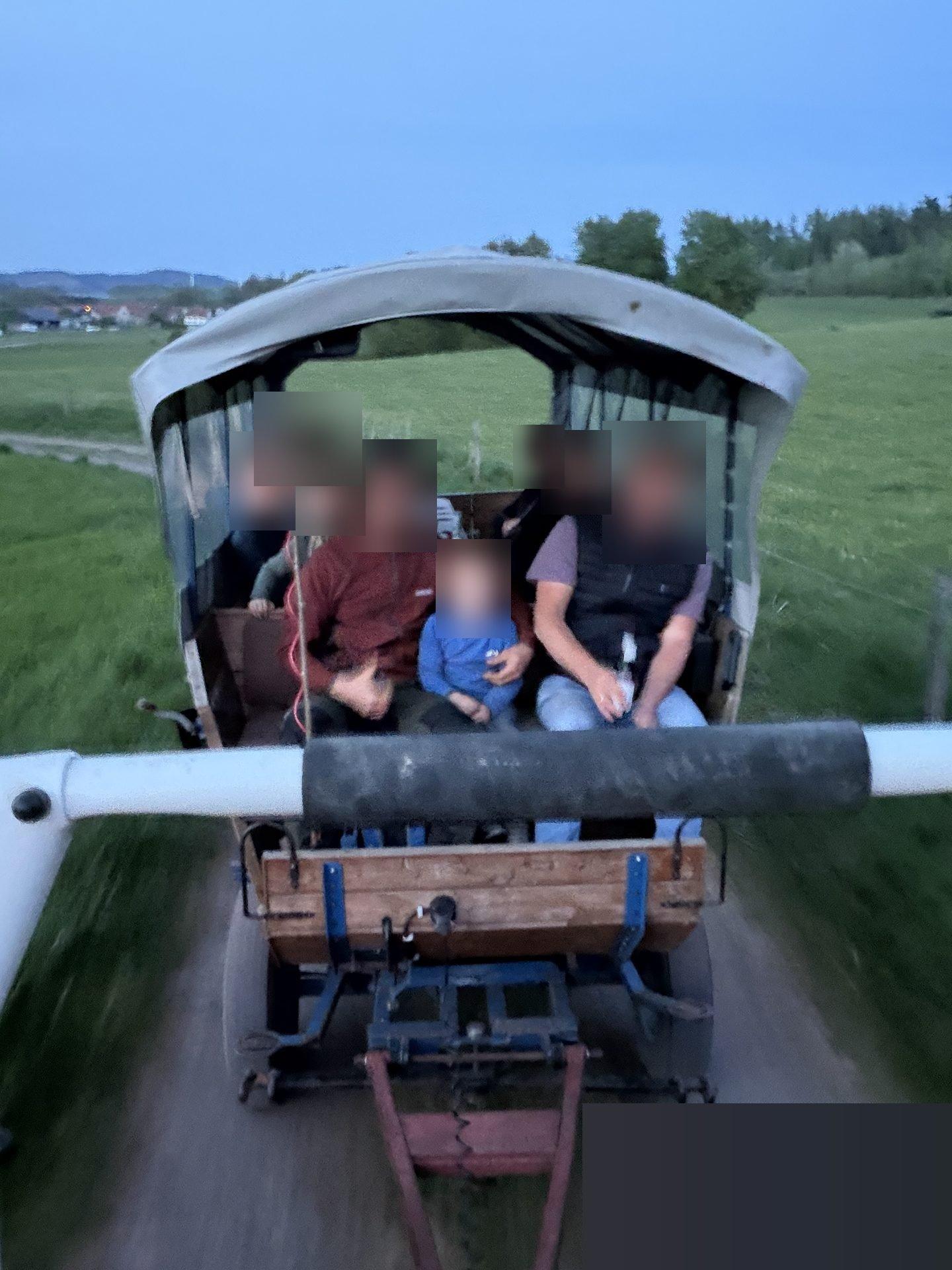 Planwagenfahrt am Abend: Gäste sitzen im überdachten Planwagen auf dem Feldweg — Hof-Erlebnis und Gemeinschaft
